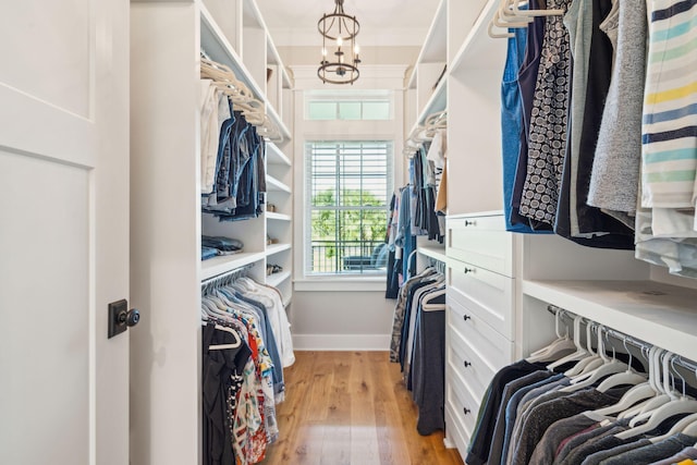 spacious closet featuring light hardwood / wood-style flooring and an inviting chandelier