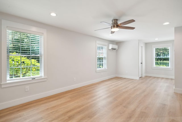 empty room featuring an AC wall unit, a wealth of natural light, light hardwood / wood-style flooring, and ceiling fan