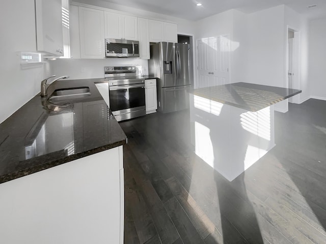 kitchen with sink, dark wood-type flooring, white cabinetry, stainless steel appliances, and dark stone counters