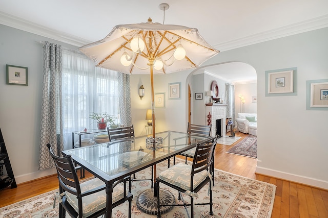 dining room with light wood-type flooring, a brick fireplace, arched walkways, and crown molding