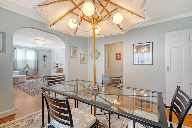 dining room featuring arched walkways, baseboards, wood finished floors, and crown molding