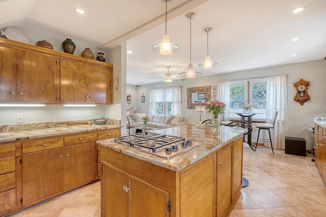 kitchen with hanging light fixtures, stainless steel gas stovetop, brown cabinetry, and a center island