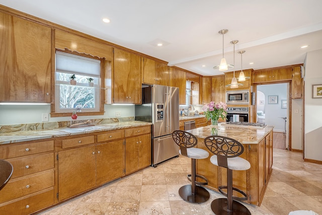 kitchen with appliances with stainless steel finishes, a center island, brown cabinetry, and a sink