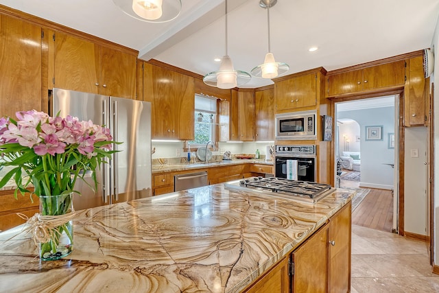 kitchen featuring arched walkways, brown cabinets, hanging light fixtures, stainless steel appliances, and a sink