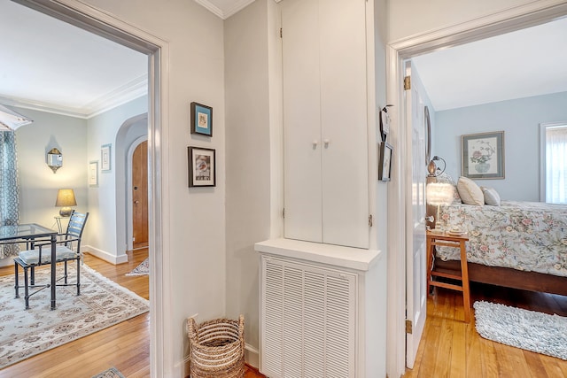 hallway featuring arched walkways, light wood finished floors, visible vents, ornamental molding, and baseboards