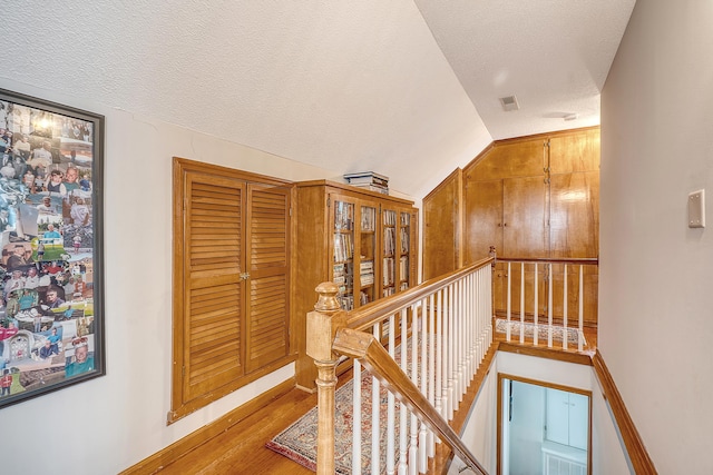 hall with visible vents, wood finished floors, vaulted ceiling, a textured ceiling, and an upstairs landing