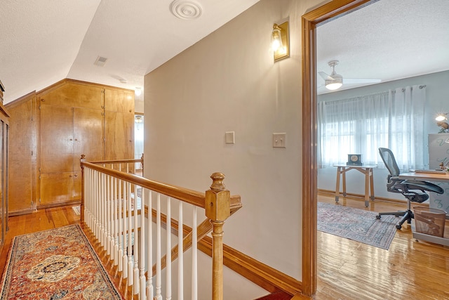 hallway featuring lofted ceiling, light wood finished floors, an upstairs landing, and a textured ceiling