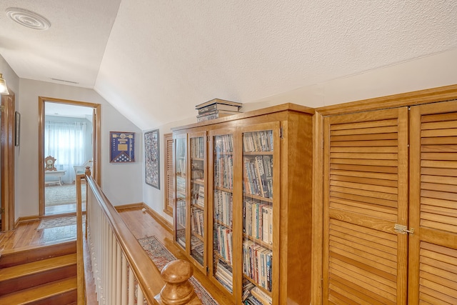 hallway featuring lofted ceiling, visible vents, a textured ceiling, an upstairs landing, and wood finished floors