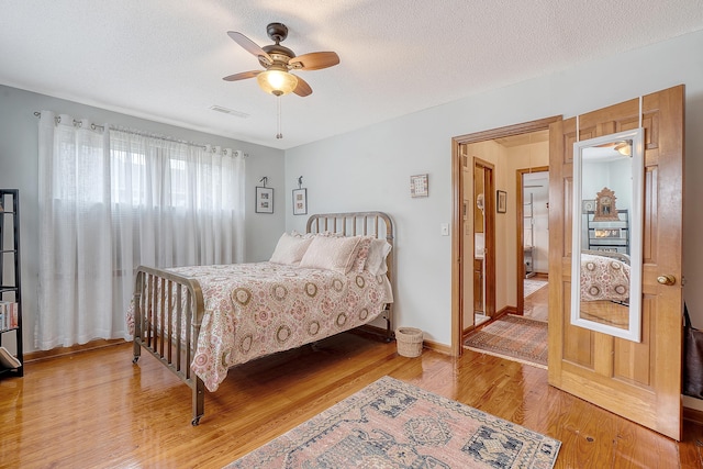 bedroom with visible vents, light wood-style flooring, a ceiling fan, a textured ceiling, and baseboards