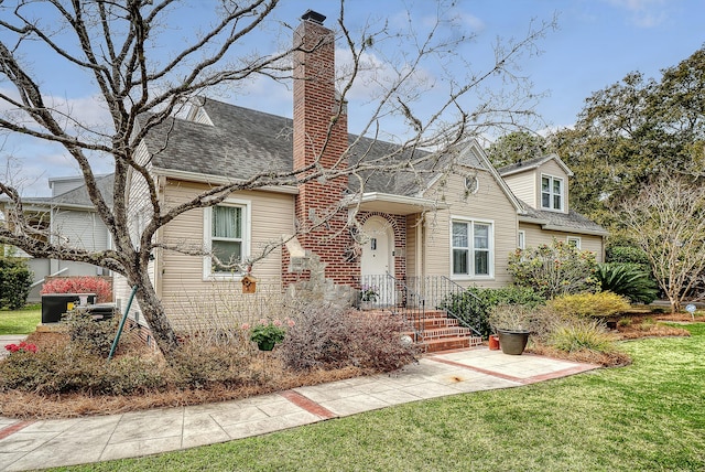 view of front of property featuring a shingled roof, a chimney, and a front lawn