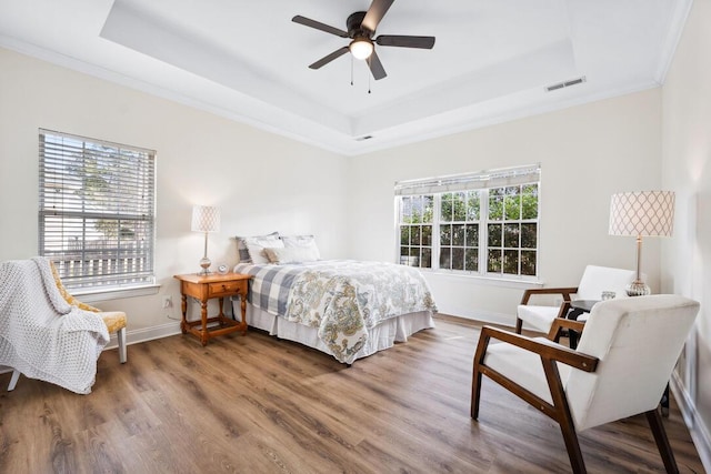 bedroom featuring baseboards, visible vents, wood finished floors, and a raised ceiling