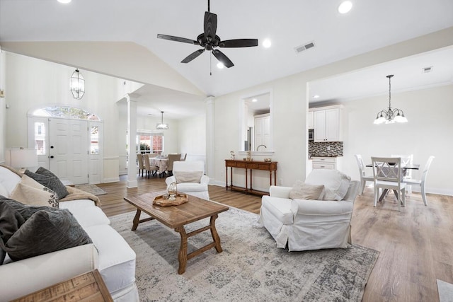 living area featuring decorative columns, visible vents, light wood-style flooring, and vaulted ceiling