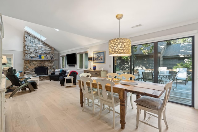 dining area featuring a stone fireplace, light hardwood / wood-style floors, and lofted ceiling