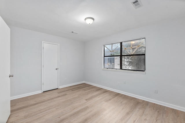 empty room with light wood finished floors, visible vents, and baseboards