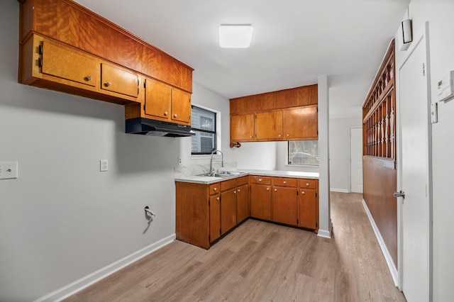 kitchen featuring light wood-style flooring, brown cabinets, light countertops, under cabinet range hood, and a sink