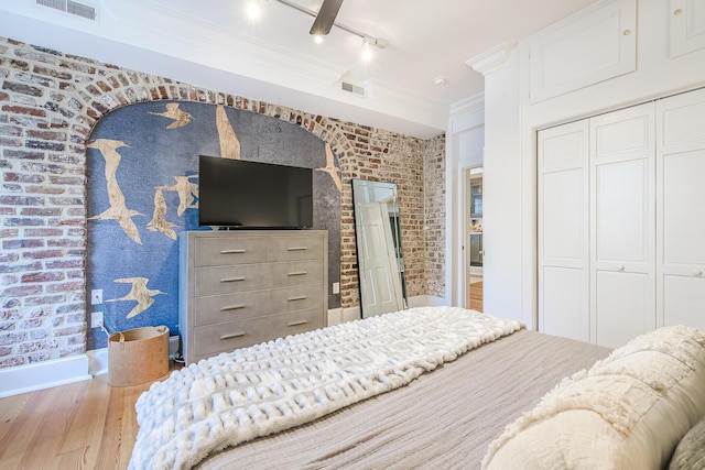 84 Bull St Unit F, Charleston, SC 29401 - bedroom featuring wood finished floors, a closet, rail lighting, brick wall, and ornamental molding