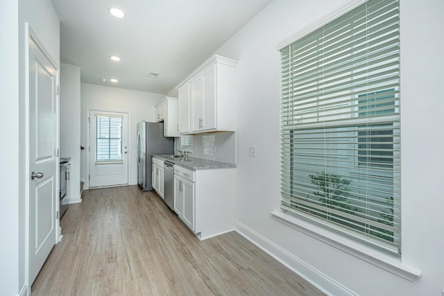 kitchen with light hardwood / wood-style floors, stainless steel appliances, backsplash, light stone countertops, and white cabinets