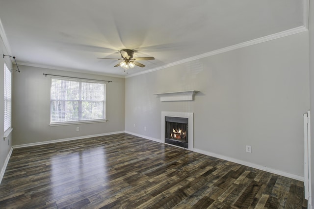 unfurnished living room with dark wood-type flooring, ornamental molding, a ceiling fan, a warm lit fireplace, and baseboards