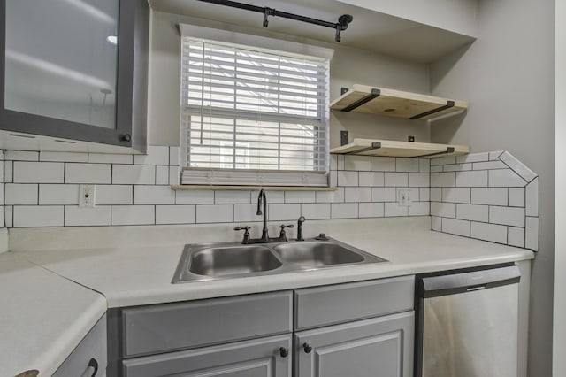 kitchen with gray cabinetry, open shelves, a sink, stainless steel dishwasher, and decorative backsplash