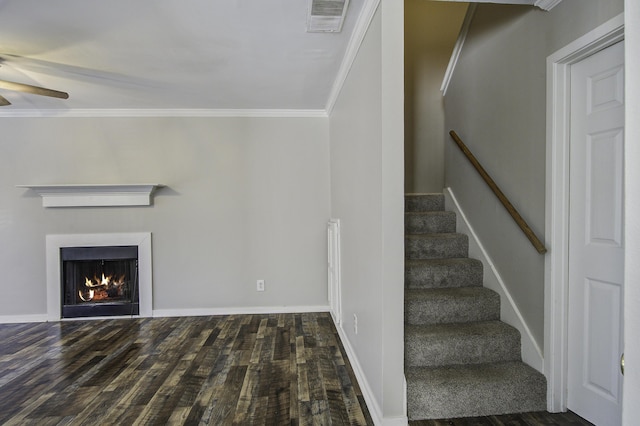 unfurnished living room with visible vents, a ceiling fan, a warm lit fireplace, wood finished floors, and crown molding