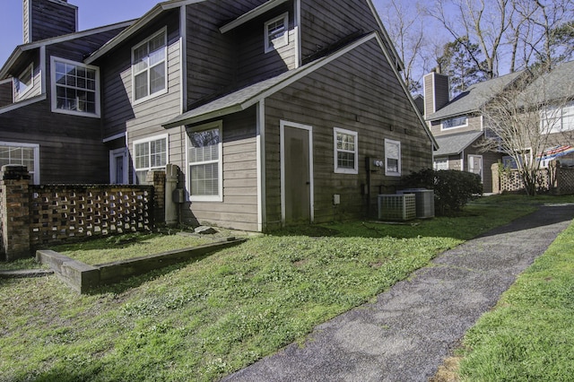 back of property with central air condition unit, a lawn, and a chimney