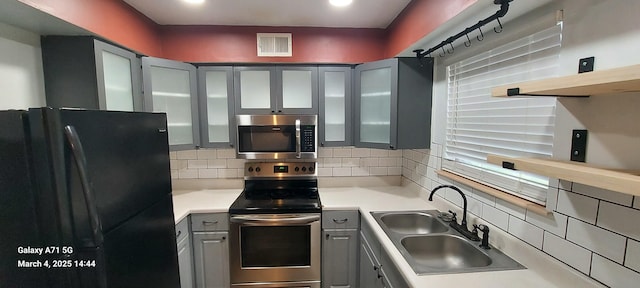 kitchen with visible vents, gray cabinets, a sink, appliances with stainless steel finishes, and decorative backsplash