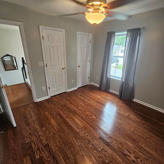 unfurnished bedroom with multiple closets, ceiling fan, and dark hardwood / wood-style flooring