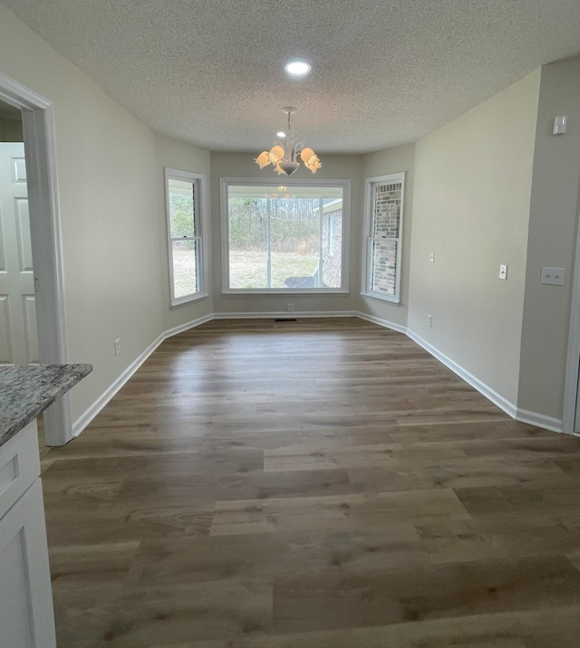 unfurnished dining area featuring dark wood-type flooring, a textured ceiling, baseboards, and an inviting chandelier