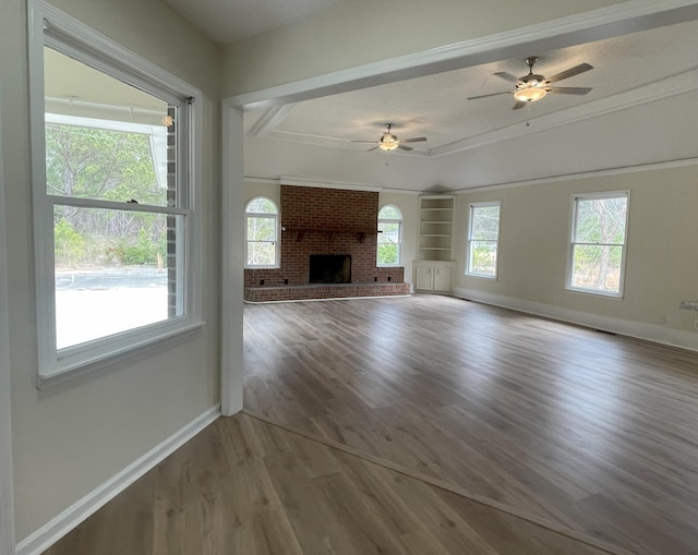 unfurnished living room with a brick fireplace, wood finished floors, a wealth of natural light, and baseboards