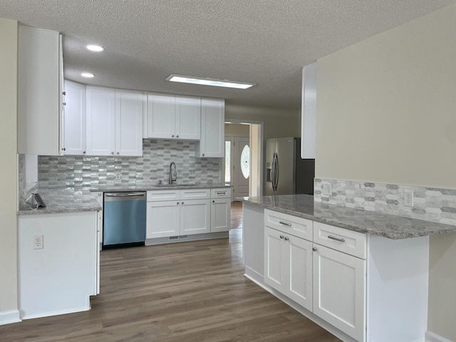 kitchen featuring dark wood-style flooring, tasteful backsplash, appliances with stainless steel finishes, white cabinets, and a sink