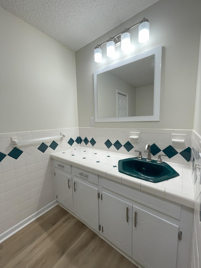 bathroom featuring tile walls, wainscoting, a textured ceiling, vanity, and wood finished floors