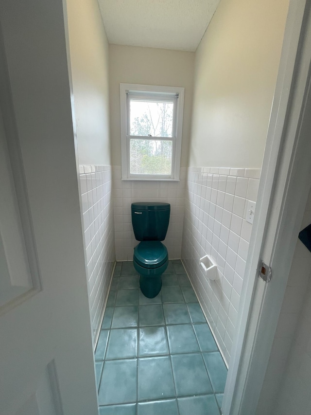 bathroom with a wainscoted wall, tile walls, toilet, and tile patterned floors