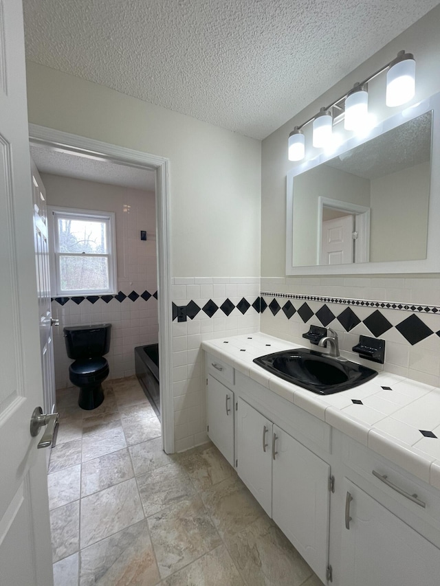 bathroom with a textured ceiling, toilet, vanity, tile walls, and a shower