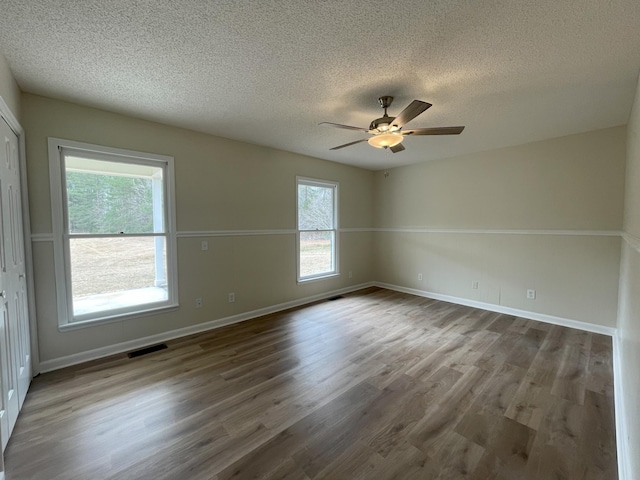 empty room featuring visible vents, a ceiling fan, a textured ceiling, wood finished floors, and baseboards