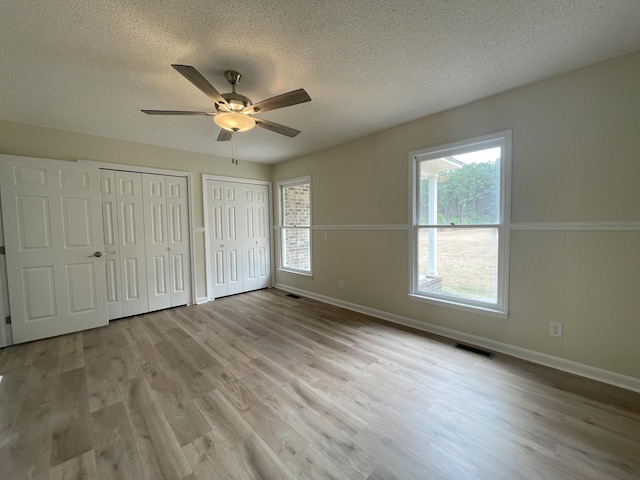 unfurnished bedroom with two closets, visible vents, a ceiling fan, a textured ceiling, and wood finished floors