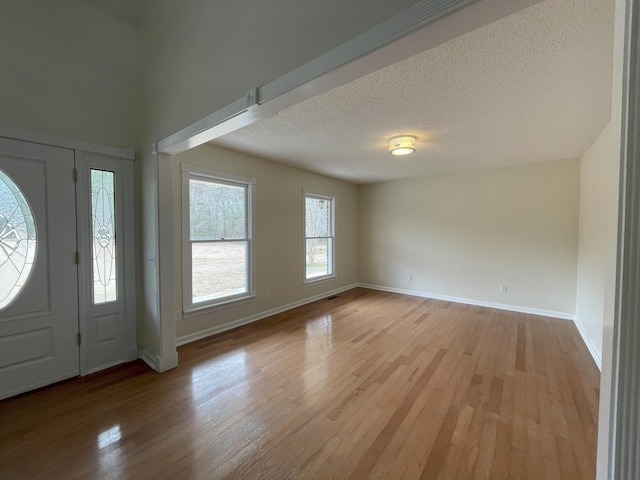 foyer entrance with a textured ceiling, light wood-type flooring, and baseboards