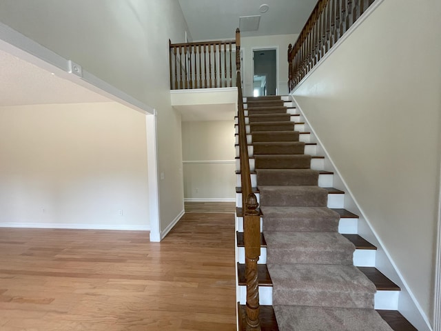 stairway with wood finished floors, a towering ceiling, and baseboards