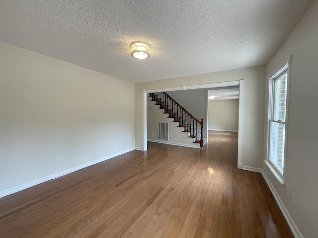 unfurnished room featuring baseboards, visible vents, stairway, wood finished floors, and a textured ceiling