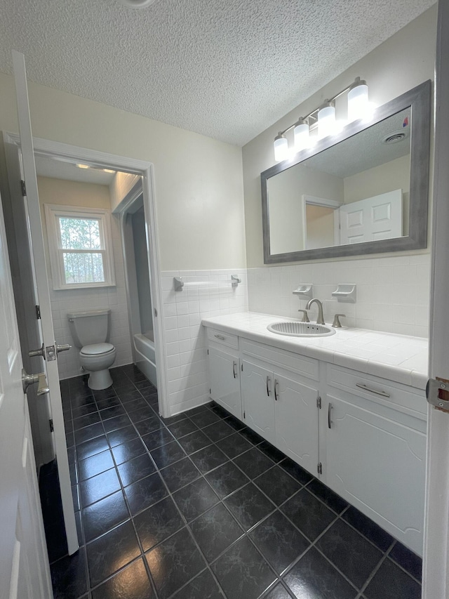 bathroom with tile walls, toilet, vanity, a textured ceiling, and tile patterned flooring