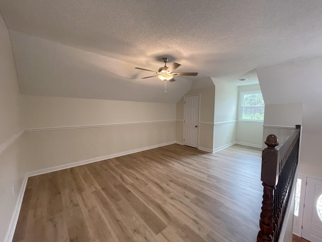 bonus room featuring vaulted ceiling, a textured ceiling, light wood-type flooring, and baseboards