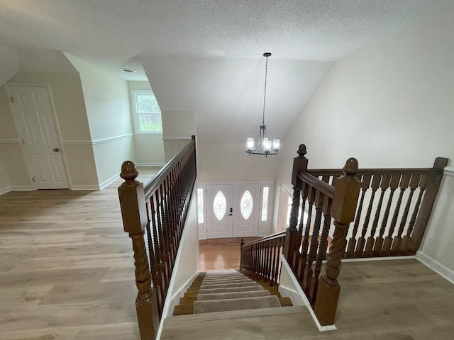 staircase featuring baseboards, a textured ceiling, a chandelier, and wood finished floors