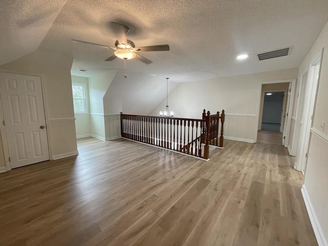 additional living space with visible vents, vaulted ceiling, a textured ceiling, wood finished floors, and baseboards