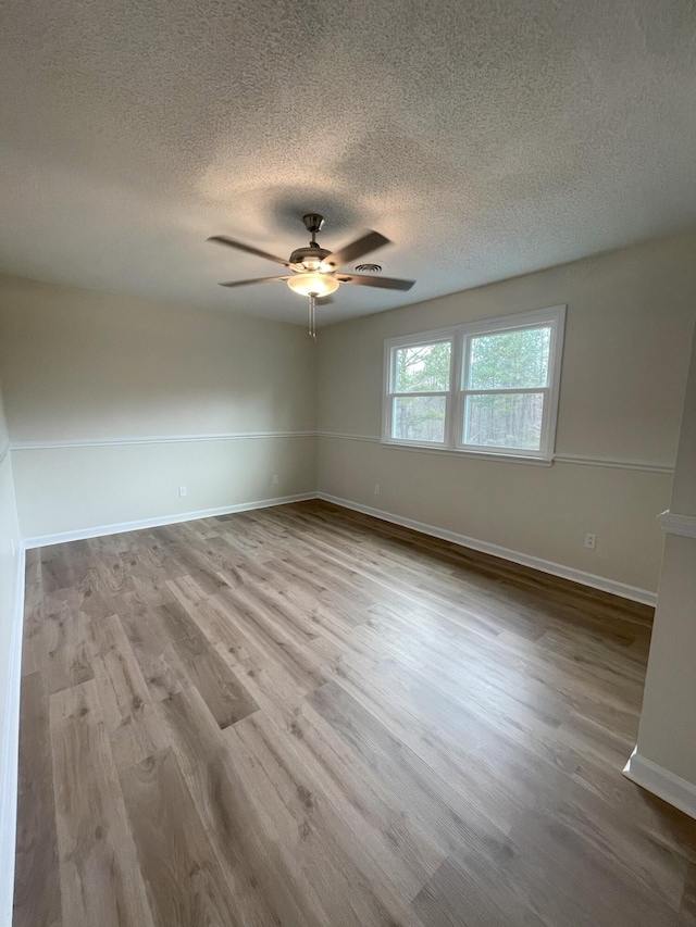 spare room featuring a textured ceiling, wood finished floors, a ceiling fan, and baseboards