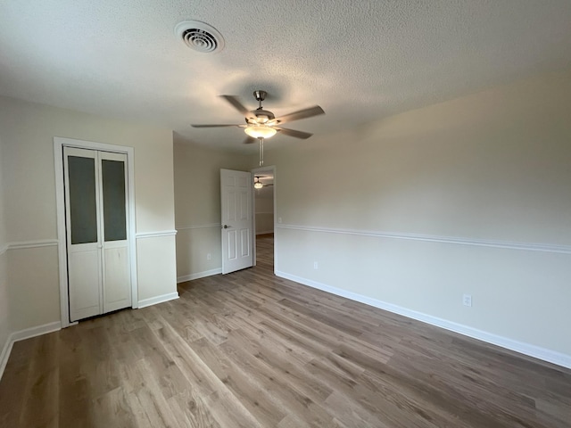 unfurnished bedroom with baseboards, visible vents, wood finished floors, a textured ceiling, and a closet