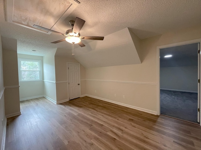 bonus room with a textured ceiling, vaulted ceiling, wood finished floors, and baseboards