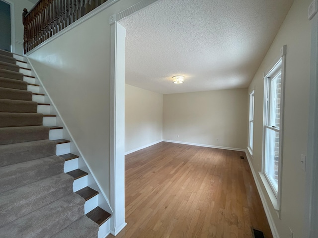 interior space with visible vents, a textured ceiling, baseboards, and wood finished floors