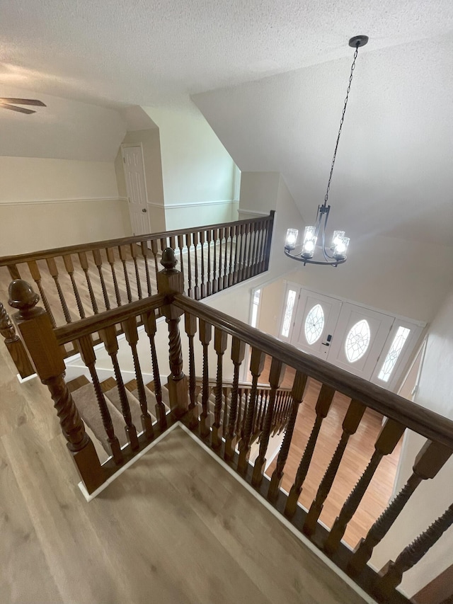 stairs with a notable chandelier, a textured ceiling, high vaulted ceiling, and wood finished floors