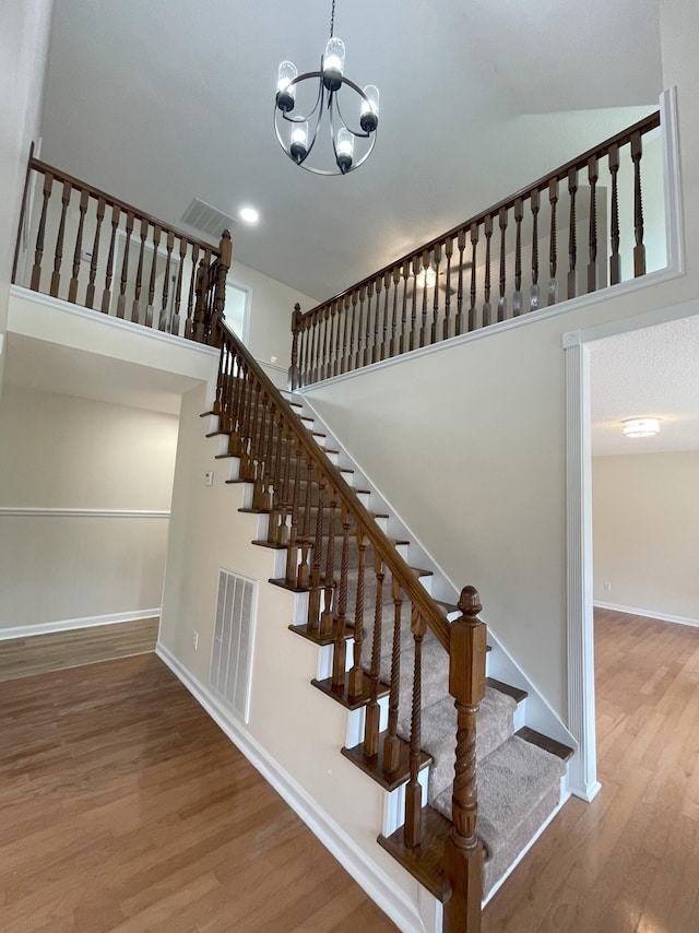 staircase featuring an inviting chandelier, visible vents, and wood finished floors