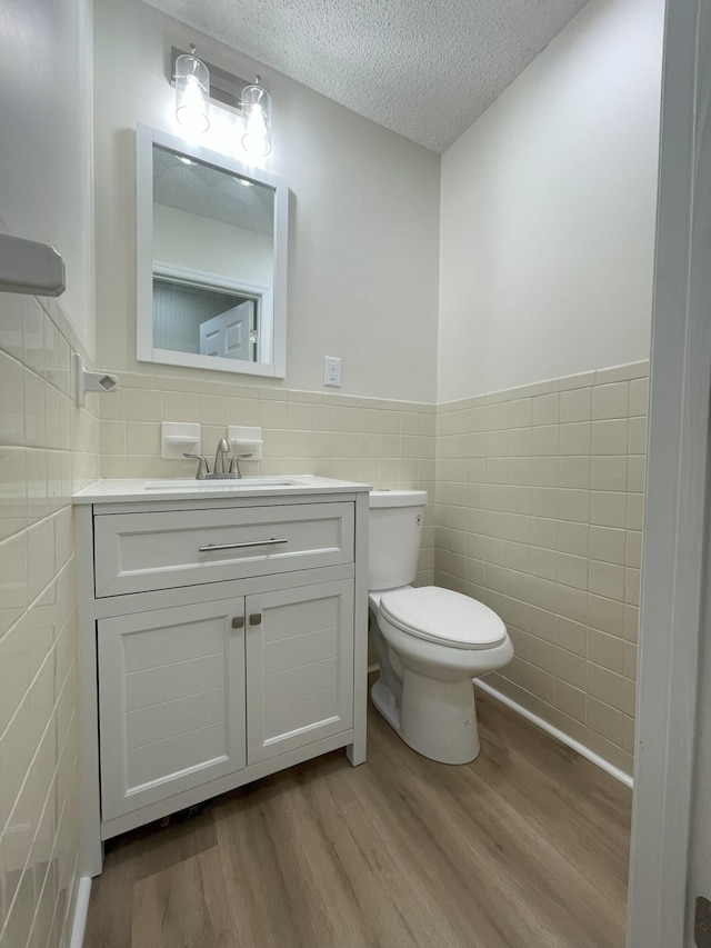 bathroom with toilet, wood finished floors, a textured ceiling, vanity, and tile walls