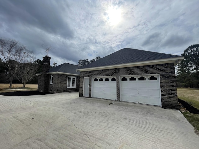 exterior space featuring an outbuilding, an attached garage, brick siding, driveway, and a chimney